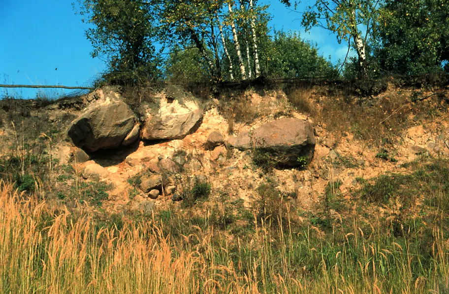 Angeschnittene Sandgrube mit großen Granitblöcken, die im sandigen Sediment stecken